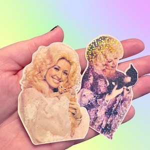 May include: Two die-cut stickers featuring a portrait of a blonde woman with voluminous hair. The left sticker shows her holding an orange kitten, while the right sticker features a holographic finish and depicts her holding a small black kitten.