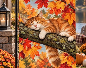 Op de afbeelding: Een rechthoekige tuin vlag met een slapende rode cyperse kat op een boomtak, omringd door levendige herfst esdoornbladeren in tinten rood, oranje en geel, opgehangen aan een zwarte metalen standaard in een buitenomgeving.