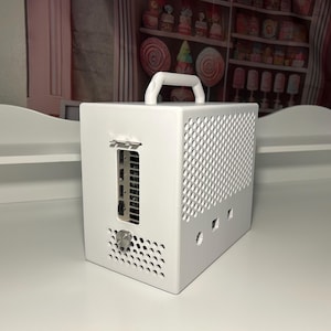 Op de afbeelding: Een witte, kubusvormige computerkast met een handvat aan de bovenkant. De kast heeft een geperforeerd zijpaneel en diverse poorten zichtbaar aan de achterkant. Het ontwerp is minimalistisch en modern, geschikt voor een desktop computer.