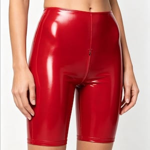 May include: Shiny red biker shorts with a front zipper. The shorts are made of a glossy material and have a fitted design. The shorts are knee-length and have a smooth, reflective surface.