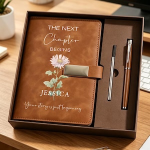 May include: A brown notebook with a magnetic closure, a matching pen, and a thin metal stylus inside a gift box. The notebook cover features a floral illustration, the text "THE NEXT Chapter BEGINS", the name "JESSICA", and "Your story is just beginning".