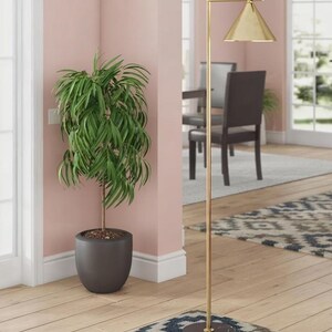 May include: A tall floor lamp with a thin gold-toned metal stand, a conical gold-toned shade, and a round black marble base. The lamp features a straight vertical pole with a right-angle arm extending to support the downward-facing light fixture.
