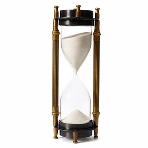Könnte beinhalten: Eine Sanduhr mit einem klaren Glaskolben, gefüllt mit weißem Sand, gehalten von einem Rahmen aus vier vertikalen, messingfarbenen, kannelierten Säulen. Die oberen und unteren Kappen sind kreisförmig und schwarz mit kleinen messingfarbenen Zierknöpfen.