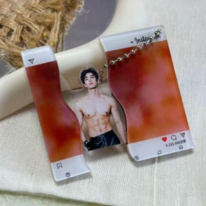May include: A clear acrylic keychain featuring a shirtless man with a muscular physique. The keychain is designed to resemble an Instagram post, with the Instagram logo and interface elements visible. The background is a gradient of orange and white.
