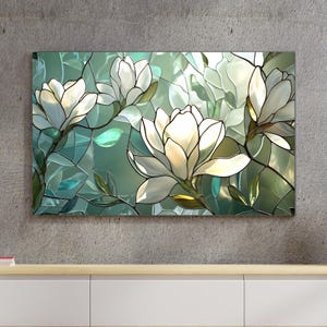 May include: A rectangular stained glass artwork featuring white magnolia flowers with green leaves and stems against a teal and green background. The artwork is mounted on a gray concrete wall.