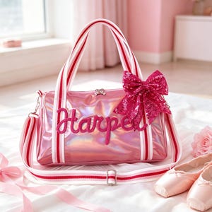 May include: A metallic pink duffel bag featuring the name Harper in dark pink script lettering on the front. The bag includes white and red striped handles and a matching adjustable shoulder strap, accented with a large, sparkly dark pink sequin bow.