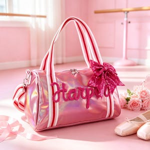 May include: Pink duffel bag with white and red striped handles and a large sequined bow. The bag has the name "Harper" embroidered on the front. Ballet shoes and roses are in the background.