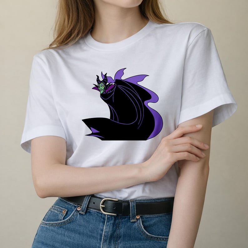 May include: White t-shirt featuring a graphic of a cartoon villain in black, purple, and green. The character has horns and a cape. The shirt is made of a soft material and is suitable for casual wear.