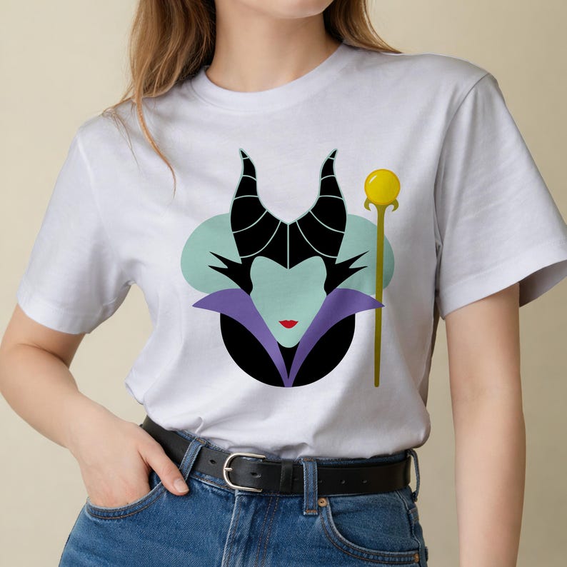 May include: White t-shirt featuring a stylized illustration of a character with black horns, a green face, and a purple collar. A gold staff with a yellow orb is to the right of the character.