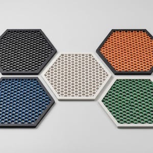 Puede incluir: Un conjunto de cinco posavasos hexagonales en varios colores: negro, naranja, verde, azul y beige. Cada posavasos presenta un patrón de panal dentro de un borde contrastante, creando un diseño moderno.