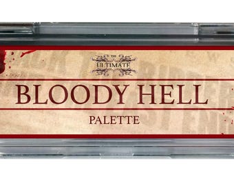 May include: A rectangular makeup palette with a clear plastic case. The label features the text "ULTIMATE BLOODY HELL PALETTE" in red and brown, with blood splatter graphics. The brand name "DASHBO" is in the lower left corner.