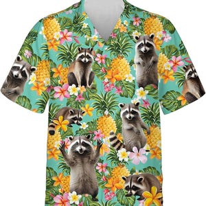 Può includere: Camicia a maniche corte con sfondo turchese. La camicia presenta un motivo ripetuto di procioni, ananas e fiori tropicali nei toni del giallo, rosa e verde. I procioni sono in varie pose.