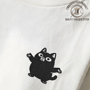 May include: White t-shirt featuring a black cartoon cat design. The shirt has a crew neck and a small label reading "novaline". An embroidered product label states "QUALITY THREAD & STITCH". A casual, comfortable garment.