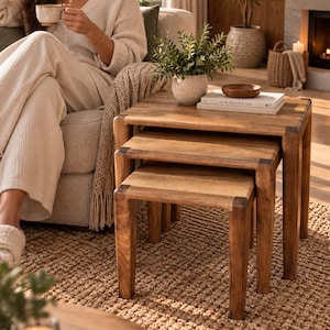 May include: A set of three nested tables crafted from medium-toned wood with a smooth finish. The tables feature a rectangular design with rounded edges on the legs and tops, stacked neatly to save space while maintaining a consistent natural grain.