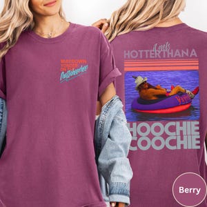 May include: Berry-colored t-shirt with the text "WAYDOWN YONDER ON Chattahoochee" on the front. The back of the shirt features a graphic of a person floating in a tube with the text "it gets HOTTER THANA HOOCHIE COOCHIE".