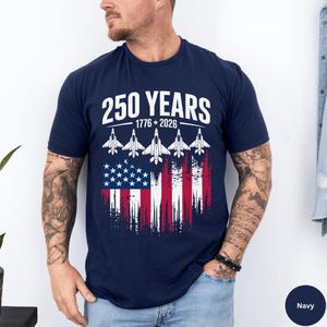 May include: Navy blue t-shirt with a graphic celebrating 250 years, 1776-2026. The design includes white jets and a distressed American flag. The shirt is a short-sleeved crew neck.