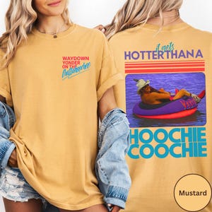 May include: Mustard-colored t-shirt with the text "WAYDOWN YONDER ON THE Chattahoochee" on the front. The back features a graphic of a person in a tube with the text "it gets HOTTER THANA HOOCHIE COOCHIE".