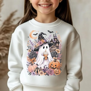 Könnte beinhalten: Ein weißes Langarm-Sweatshirt mit einem Grafikdruck eines Geistes, der einen Hexenhut trägt und ein Getränk hält, umgeben von Kürbissen, Blumen, Fledermäusen und der Silhouette eines Spukhauses. Dazu werden blaue Jeans getragen.