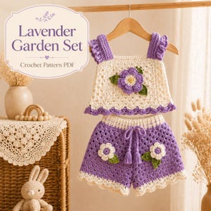 Peut inclure: Un modèle de crochet PDF intitulé Lavender Garden Set présentant un ensemble deux pièces sur un cintre en bois. L'ensemble comprend un haut crème avec une grande fleur violette et des bretelles à volants, et un short violet avec des fleurs blanches.
