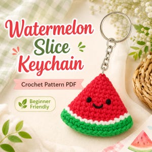 May include: A crochet watermelon slice keyring with a red triangular body, a white rind, and a green outer edge. The face features two black embroidered eyes and a smiling mouth. It is attached to a silver metal ring and chain.