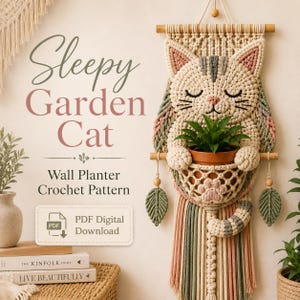 May include: A macrame wall hanging featuring a cream-colored cat with closed eyes, holding a terracotta pot with a green plant. The piece includes wooden dowels, hanging leaf accents, and multi-colored fringe. Text reads Sleepy Garden Cat.