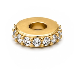 May include: A gold-colored charm with a circular design. The charm features a ring of clear, sparkling gemstones around the outer edge. The center of the charm has a large, open hole. The charm is set against a white background.