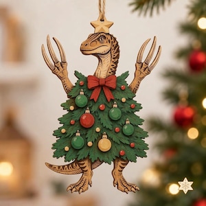 May include: A wooden Christmas tree ornament shaped like a dinosaur wearing a green pine tree costume. The dinosaur has tan skin, raised arms with claws, and a star on its head. The tree is decorated with a red bow and small red, green, and gold baubles.
