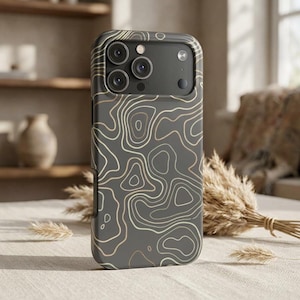 May include: A dark gray phone case with a topographic map design in shades of gold and white. The case has a raised edge around the camera lenses and a smooth, matte finish. The case is designed to fit a smartphone.