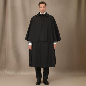 Puede incluir: Un conjunto de capa y abrigo negros. La capa es una prenda más corta, a la altura de los hombros, mientras que el abrigo llega hasta los tobillos. El atuendo se combina con pantalones negros, una camisa blanca con cuello y zapatos negros. El estilo general es formal.