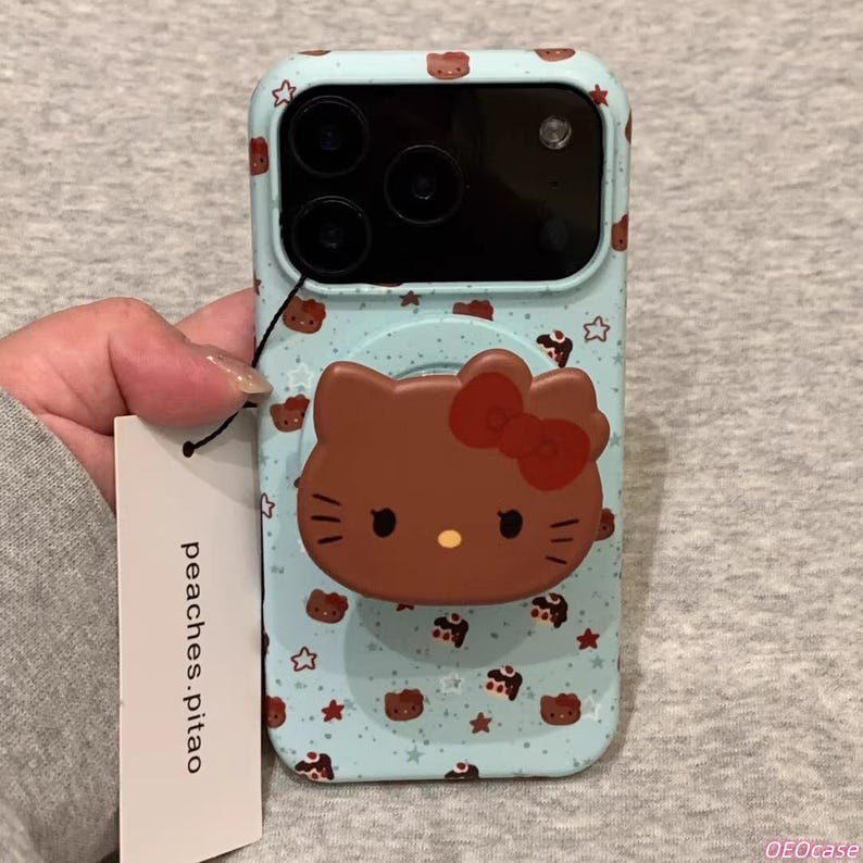May include: A light blue phone case featuring a brown Hello Kitty design with a red bow. The case has a repeating pattern of brown Hello Kitty faces and stars. The brand tag reads "peaches.pitao".