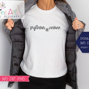 Może przedstawiać: Biały t-shirt z napisem "python mom" i małym wzorem kwiatka. Koszulkę nosi osoba w czarno-białej kratkowanej kurtce.