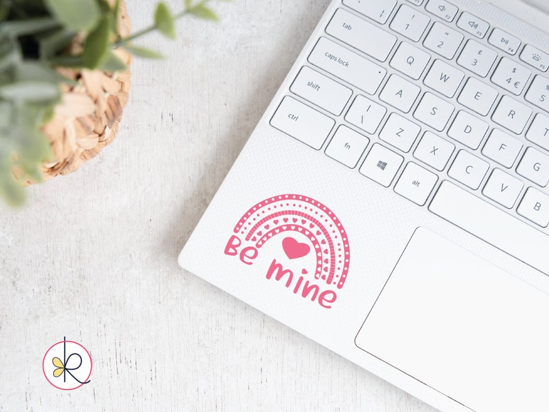May include: A pink and white rainbow sticker with a heart in the center and the text "Be mine" on a white laptop.