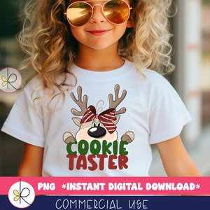 May include: A white t-shirt with a cartoon reindeer wearing a red and white bow. The reindeer is holding a cookie and the text "Cookie Taster" is written below the reindeer.