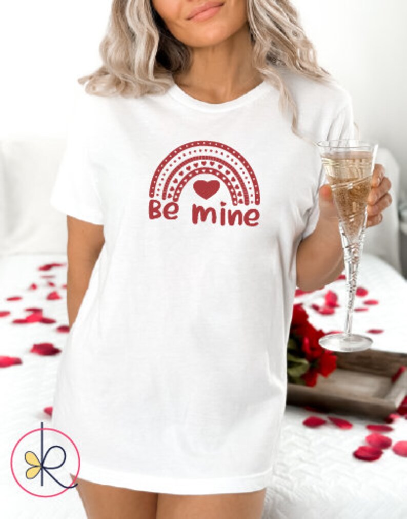 May include: White t-shirt with a red rainbow design and the text "Be mine" printed on the front.