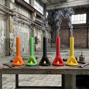 May include: Five conical incense burners in orange, green, black, red, and yellow, each featuring a small LED candle inside the base and a thin stream of smoke rising from the top, arranged in a row on a weathered wooden workbench.