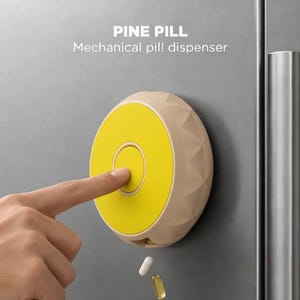 May include: A round, beige mechanical pill dispenser with a bright yellow circular button center, mounted on a metallic surface. The text PINE PILL Mechanical pill dispenser is visible above. Two pills are falling from the bottom of the device.