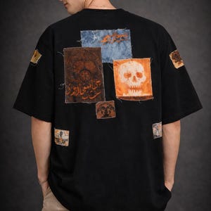 May include: Black oversized t-shirt with multiple patches. The patches feature various designs, including a skull, text, and abstract art. The shirt has a relaxed fit and short sleeves. The patches are in shades of orange, brown, and blue.