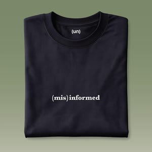 May include: A folded black t-shirt with the text "(un) (mis)informed" printed in white. The shirt has a crew neck and short sleeves. The background is a solid olive green.