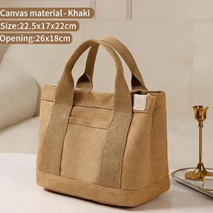May include: Khaki canvas tote bag with two handles and a front pocket. The bag measures 22.5cm x 17cm x 22cm, with an opening of 26cm x 18cm. The text "Canvas material - Khaki" is visible on the image.