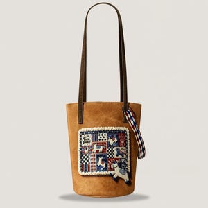 May include: A tan tote bag with brown handles and a decorative patch featuring a patchwork design with horses and the text "GET RICH QUICKLY". A small horse charm hangs from the bag.