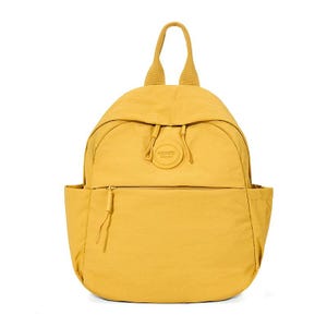 May include: Mustard yellow backpack with a rounded shape. Features a top handle, a front zippered pocket, and side pockets. The backpack has a drawstring closure and a small, circular logo on the front. The material appears to be a lightweight, durable fabric.