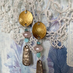 May include: Gold and silver tone earrings with pink and blue beads. The earrings feature a round disc with a textured surface and a teardrop-shaped pendant.