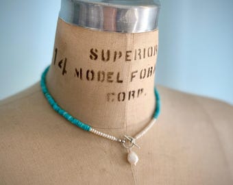 Könnte beinhalten: Eine Türkis- und Perlenkette mit Silberverschluss und einem einzelnen Perlenanhänger. Die Kette wird auf einer Vintage-Schneiderpuppe mit dem Text "SUPERIOR MODEL FOR CORP." präsentiert.