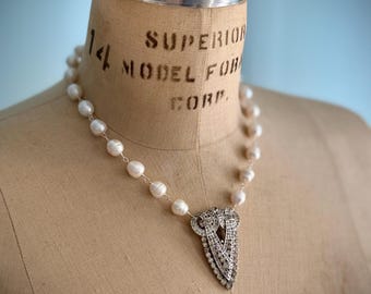 Könnte beinhalten: Eine Perlenkette mit einem silbernen Anhänger. Der Anhänger hat ein geometrisches Design mit hellen und dunklen Steinen. Die Kette wird auf einer Vintage-Schneiderpuppe mit dem Text "SUPERIOR MODEL FOR CORP." präsentiert.