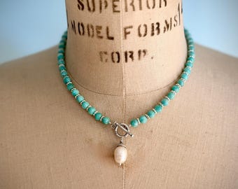 Könnte beinhalten: Türkisfarbene Perlenkette mit Silberverschluss und einem Anhänger aus weißer Perle. Die Halskette wird auf einer Vintage-Schneiderpuppe präsentiert. Die Schneiderpuppe trägt den Text "SUPERIOR MODEL FORMS CORP."