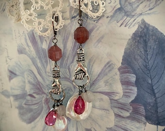 Könnte beinhalten: Hängeohrringe im Vintage-Stil. Jeder Ohrring hat eine facettierte, rotbraune Perle, einen silberfarbenen Handanhänger und einen tropfenförmigen rosa Edelstein. Die Ohrringe enthalten auch eine weiße, irisierende Perle und eine kleinere, klare Perle.