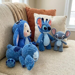 K&ouml;nnte beinhalten: Eine Sammlung von vier handgefertigten H&auml;kel-Pl&uuml;schtieren aus blauem und hellblauem Garn. Drei Figuren &auml;hneln der Figur Stitch mit gro&szlig;en Ohren, dunklen Augen und hellblauen B&auml;uchen, w&auml;hrend eine Figur ein blaues Pl&uuml;schtier mit Kapuze ist.