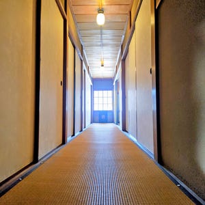 Könnte beinhalten: Ein langer, schmaler Flur mit Tatami-Mattenboden und Schiebetüren. Die Decke hat sichtbare Holzbalken und hängende Leuchten. Am Ende des Flurs befindet sich ein Fenster mit blauem Rahmen.