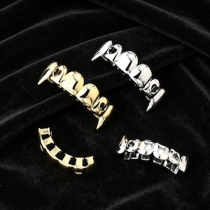 May include: Four sets of gold and silver-colored grillz, dental jewelry, are displayed against a black background. Two sets are gold, and two are silver. The grillz are designed to fit over teeth, with various tooth shapes.