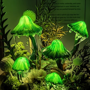 Pu&ograve; includere: Un gruppo di sculture di funghi verdi luminosi dall'aspetto vetroso. I funghi sono circondati da varie piante e fiori verdi, creando un'esposizione stravagante e illuminata. I cappelli hanno un effetto strutturato e gocciolante.
